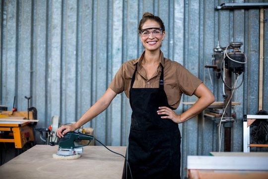 Portrait of female carpenter standing with polishing machine
