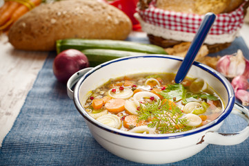 Vegetable soup in a metal bowl on a rural rustic wooden table.