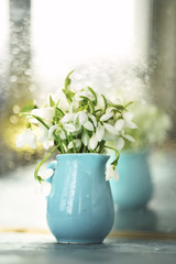 tender spring flowers snowdrops in drops of water in a blue small vase. Tender spring artistic photo. Selective soft focus.

