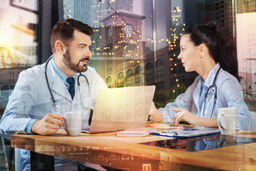 Talking doctors. Calm bearded experienced doctor sitting in front of a modern laptop with a cup of...