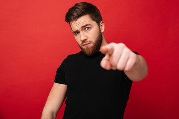 Image of muscular strict man 30s wearing casual black t-shirt posing on camera with pointing finger...