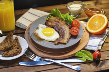 English Breakfast: fried egg with bacon, orange juice, tomatoes, zernovoi bread, lettuce leaf, top view.