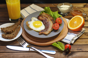 English Breakfast: fried egg with bacon, orange juice, tomatoes, zernovoi bread, lettuce leaf, top view.