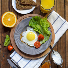 English Breakfast: fried egg, juice, cherry tomatoes, lettuce, grain bread, sauce, top view.
