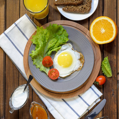 English Breakfast: fried egg, juice, cherry tomatoes, lettuce, grain bread, sauce, top view.