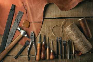 Set of leather craft tools on wooden background. Workplace for shoemaker. Piece of hide and working...