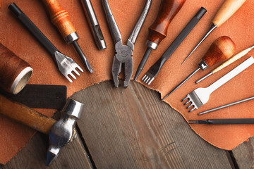 Set of leather craft tools on wooden background. Workplace for shoemaker. Piece of hide and working handmade tools on a work table.