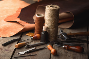 Set of leather craft tools on wooden background. Workplace for shoemaker. Piece of hide and working handmade tools on a work table.