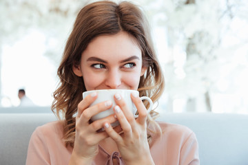 Portrait of a pleased young woman holding cup of coffee