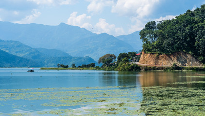 Fototapeta na wymiar Shoreline of the lake with some green algae on the surface in Pokhara region, Nepal.