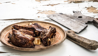 Homemade pork ribs on clay plate on white wooden background with cracked paint. Close-up.