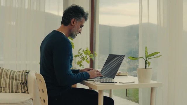 Mature man with laptop working in home office.