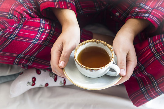 A girl sitting in pajamas from the bed holds a cup of hot tea. Morning home concept