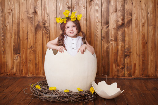 A little girl sits in an egg and holds a shell. Sunday, easter.