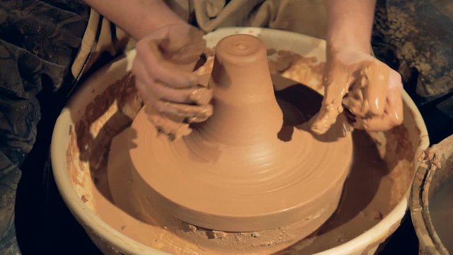 A potter uses both hands to throw clay into a tall vase. 