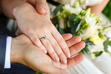 Obraz na płótnie Canvas Bride and groom's hands with wedding rings and bouquet of flowers