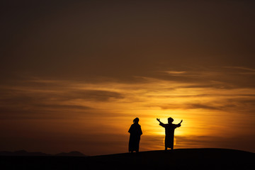 Fototapeta na wymiar Silhouette of two berber in desert Sahara, Morocco with beautiful and colorful sunset in background