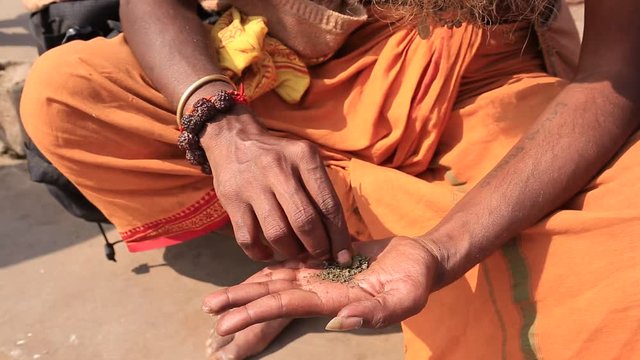 Hindu sadhu man preparing a cigarette to smoke marijuana with chillum on the ghats of the Ganges river in Varanasi, India . Close up