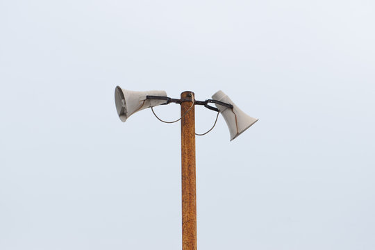 Old outdoor white loudspeakers, megaphones on a rusty metal pole. - Powered by Adobe