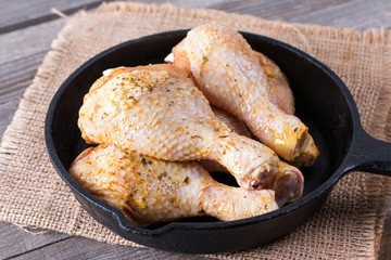 Raw chicken legs in a frying pan on a wooden table. Meat ingredients for cooking.