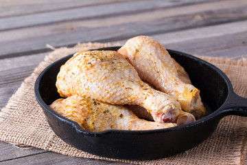 Raw chicken legs in a frying pan on a wooden table. Meat ingredients for cooking.