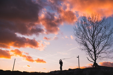 Man silhouette with whip, sunset sky in background