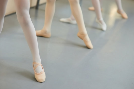 Legs of ballerinas in dance position. Young ballet dancers performing dance move at class, cropped image.