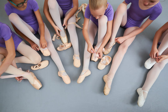 Group of ballerinas put on slippers, top view. Young ballerinas putting on pointe shoes while sitting on the floor. Preparation for dance lesson.