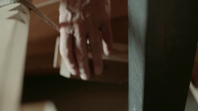 close up of the hand of an old caucasian man inspects a wooden beam where dusts falls off that hangs by a leather strap inside a dutch wind mill shot in 50fps slowmotion