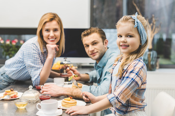 parents and little daughter having breakfast together at home