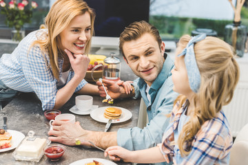parents and little daughter having breakfast together at home