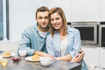 portrait of smiling couple sitting at table with breakfast at home