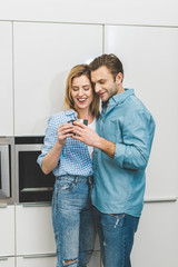 portrait of couple with cup hugging in kitchen at home