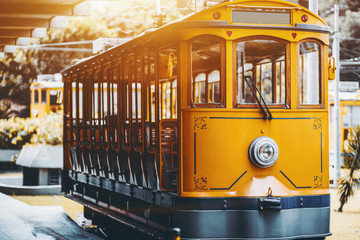 View of empty yellow glossy excursion tram waiting at tramway station in Rio de Janeiro: single headlight, opened interior with wooden windows and seats inside, shallow depth of field, sunny day - obrazy, fototapety, plakaty