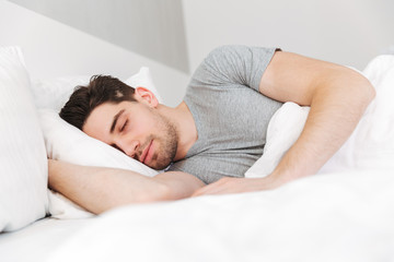 Portrait of handsome man having stubble and wearing casual clothes, sleeping at home in bed with white bedding