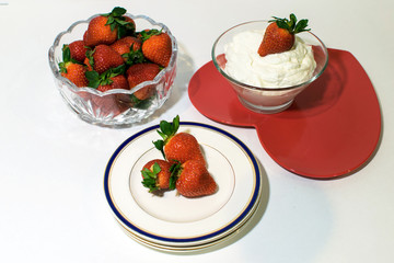 A bowl of strawberries, and strawberries on cream and plates