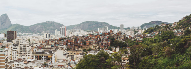 Panoramic image of Rio de Janeiro favelas district surrounded by hills and modern office and residential houses; a pronounced tendency towards social differentiation: poor buildings among regular ones