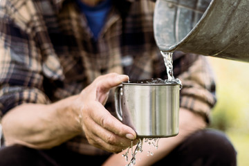 Man is holding a steel mug and a well  water is pouring from a bucket, life and thirst concept