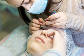 A young girl increases eyelashes in a beauty salon. The process of increasing and volumetric eyelash extensions to a blonde girl.
