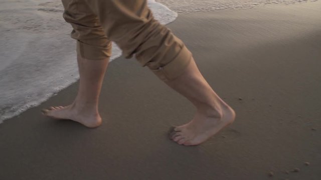 Businessman walking bare foot on sandy beach near the sea, after work.