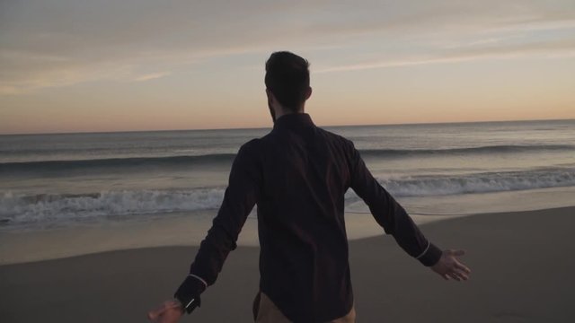Business man walking on beach at sunset, after work. 4K slow motion.