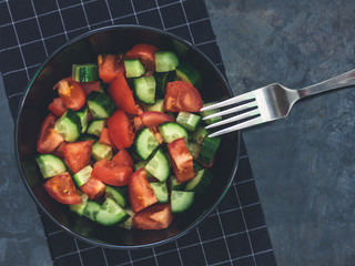 Fresh cucumber tomato salad on black background. Healthy food. A vegetarian salad. Fresh vegetables. Top view. Dark moody