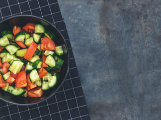 Fresh cucumber tomato salad on black background. Healthy food. A vegetarian salad. Fresh vegetables. Top view. Dark moody