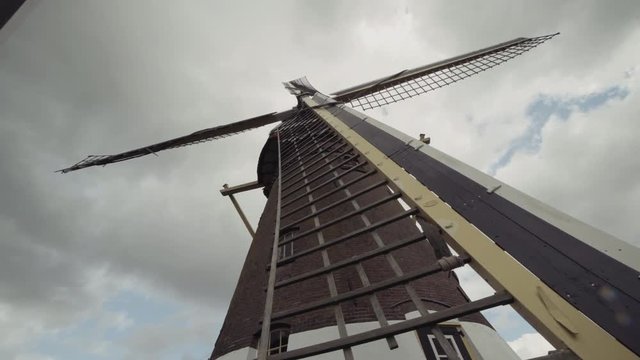 Extreme wide angle low angle shot of an old Dutch crafted windmill starting up and start spinning much faster with open sails on a grey day