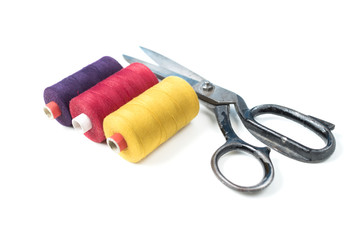 Colored sewing thread coils with old metal scissors on white background