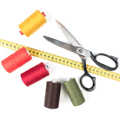 Sewing thread coil with old metal scissors and yellow measuring tape on white background