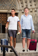 Fototapeta na wymiar Men travelers with luggage heading to hotel on foot