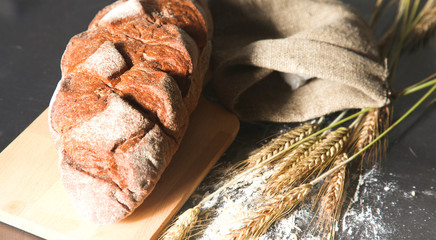 rustic crusty bread and wheat ears on a dark wooden table