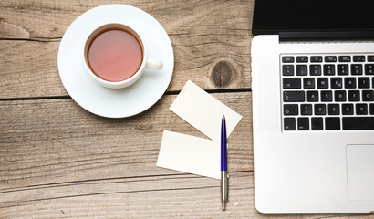 Blank business cards with pen, laptop and tea cup on wooden office table
