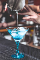 The barman mixes cocktail in a glass for martini on a bar counter